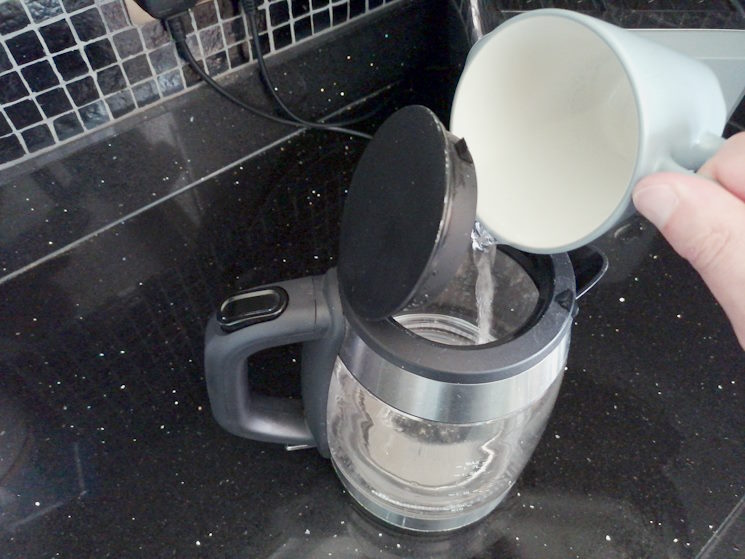 Pouring water from cup into a kettle
